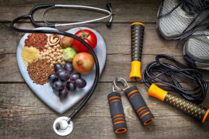 A heart-shaped plate of nuts, fruit and vegetables next to a stethoscope and various fitness equipment