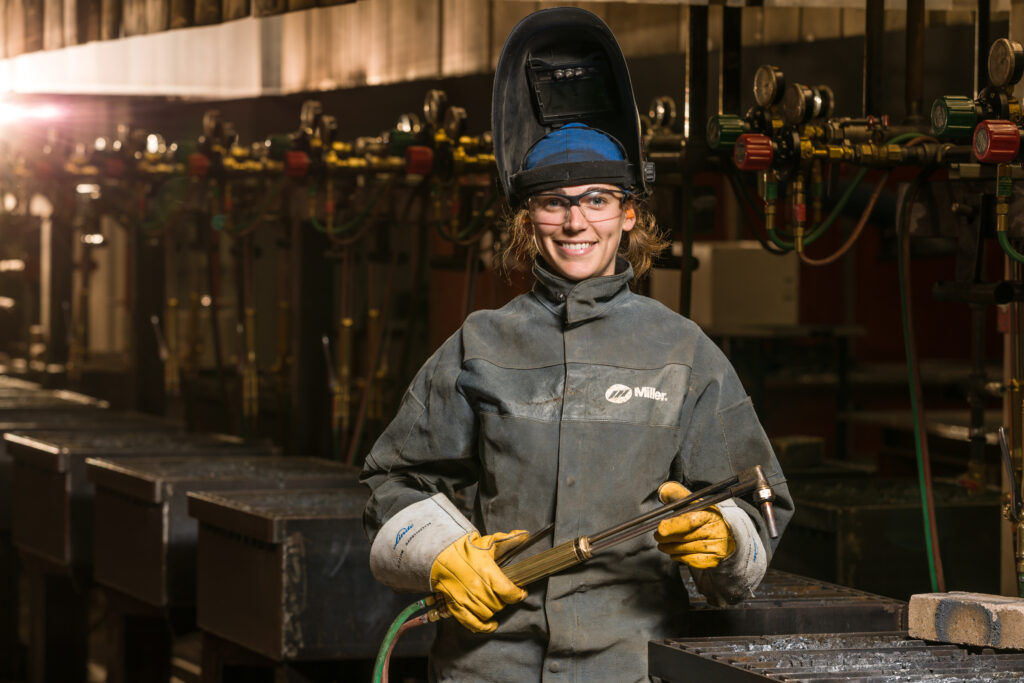 Female welder wearing protective gear and a raised face shield