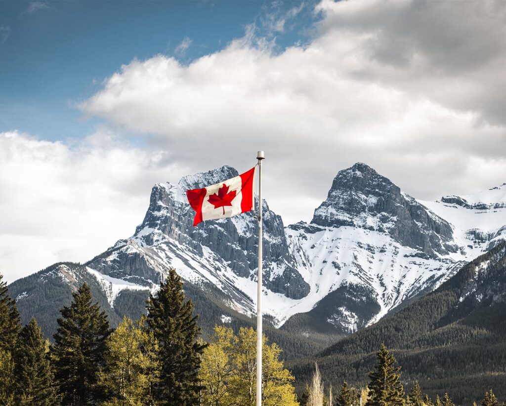 Landscape photograph of snowy mountains with the Canadian flag in the foreground